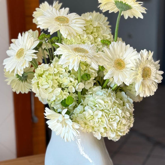 Ramo de gerberas blancas con hortensias verde claro y crisantemos verdes en jarrón de cerámica blanca