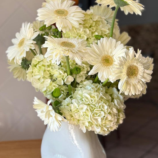 Ramo de gerberas blancas con hortensias y crisantemos verdes en jarrón de cerámica blanca con relieve de flor