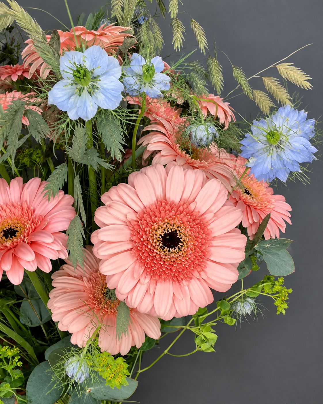 Detalle de ramo con gerberas color melocotón, nigella azul, espigas de avena y bupleurum