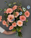 Ramo grande de gerberas color melocotón con nigella azul y blanca, bupleurum y eucalipto, sostenido en la mano