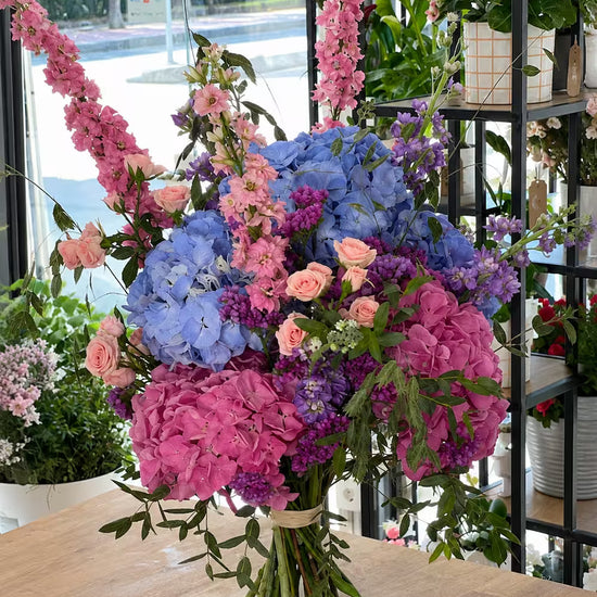 Ramo de hortensias azules y rosas con delphinium, mini rosas melocotón y limonium morado en el estudio floral