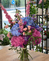 Ramo de hortensias azules y rosas con delphinium, mini rosas melocotón y limonium morado en el estudio floral
