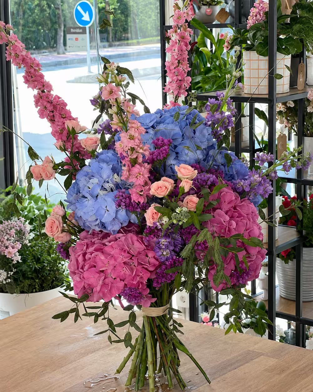 Ramo de hortensias azules y rosas con delphinium, mini rosas melocotón y limonium morado en el estudio floral