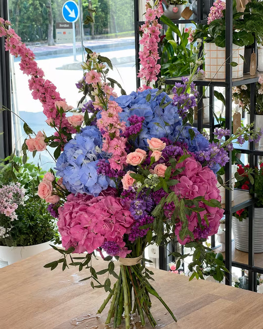 Ramo de hortensias azules y rosas con delphinium, mini rosas melocotón y limonium morado en el estudio floral