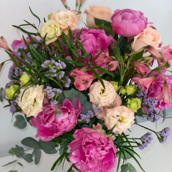 Ramo de peonías fucsia con lisianthus crema, rosas melocotón, alstroemerias rosas y limonium lila