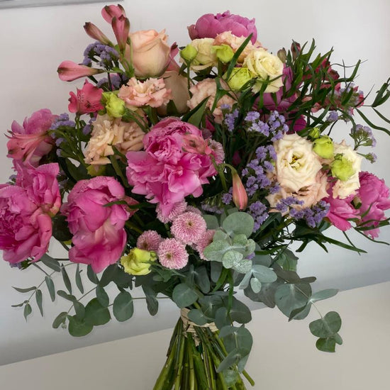 Ramo de peonías fucsia, rosas melocotón, alstroemerias y limonium lila con eucalipto, atado con rafia