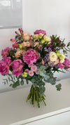 Ramo de peonías fucsia, rosas melocotón, alstroemerias y limonium lila con eucalipto, atado con rafia