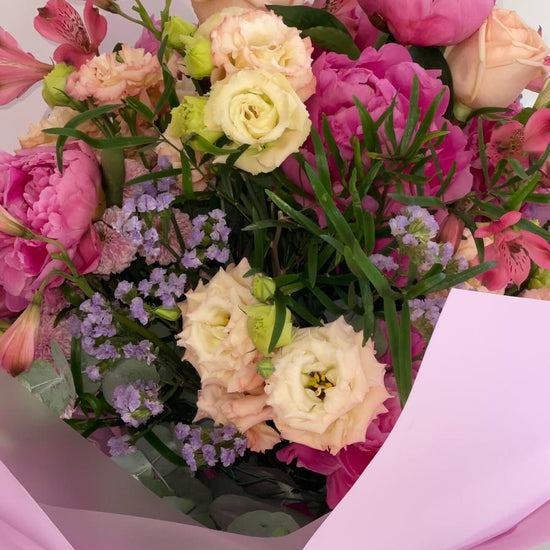 Ramo de peonías fucsia y lisianthus crema con alstroemerias y limonium lila, envuelto en papel rosa con cintas