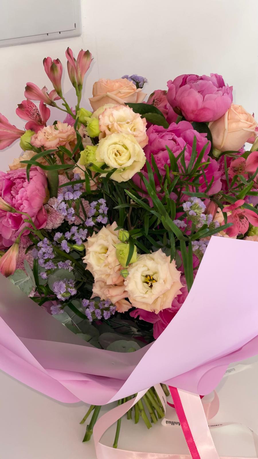 Ramo de peonías fucsia y lisianthus crema con alstroemerias y limonium lila, envuelto en papel rosa con cintas