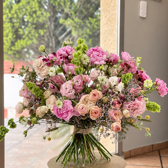 Ramo de peonías rosas, lisianthus, rosas ramificadas melocotón y molucela sobre mesa redonda