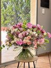 Ramo de peonías rosas, lisianthus, rosas ramificadas melocotón y molucela sobre mesa redonda