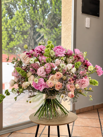 Ramo de peonías rosas, lisianthus, rosas ramificadas melocotón y molucela sobre mesa redonda