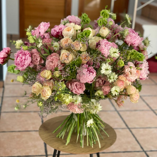 Ramo grande de peonías rosas, rosas de jardín crema, lisianthus y nigella sobre mesa redonda