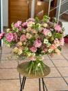 Ramo grande de peonías rosas, rosas de jardín crema, lisianthus y nigella sobre mesa redonda