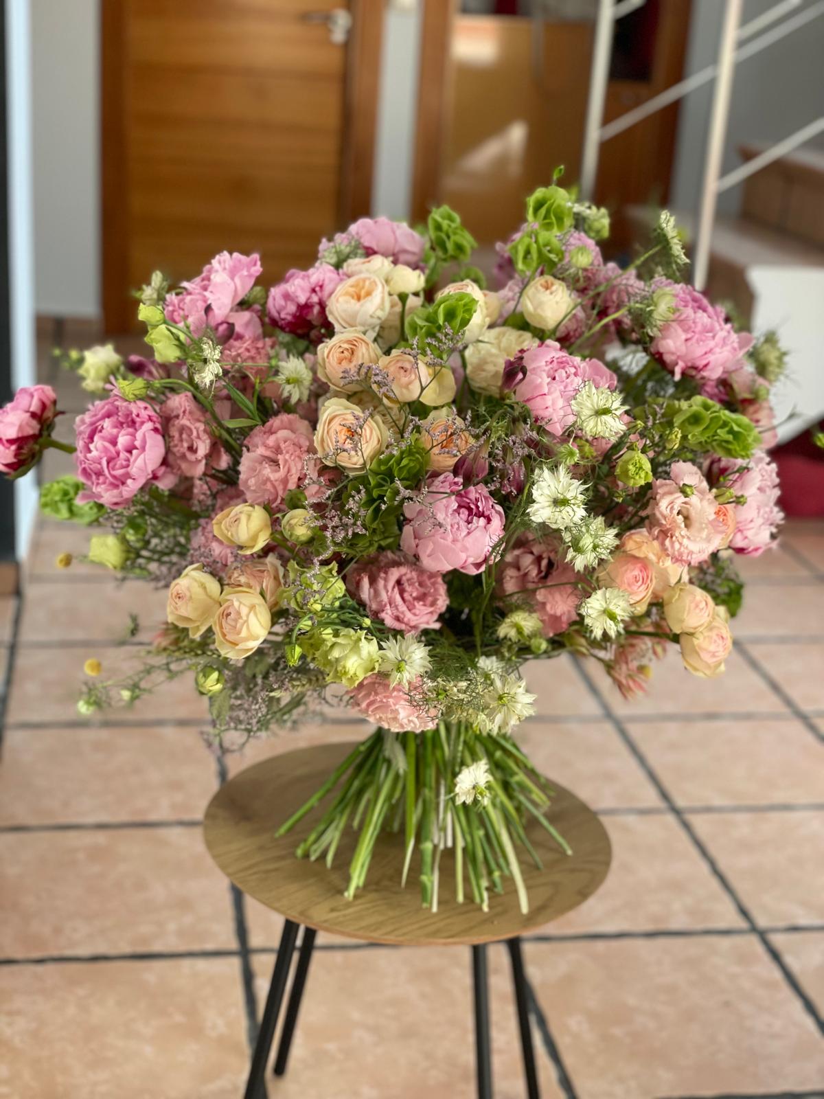 Ramo grande de peonías rosas, rosas de jardín crema, lisianthus y nigella sobre mesa redonda