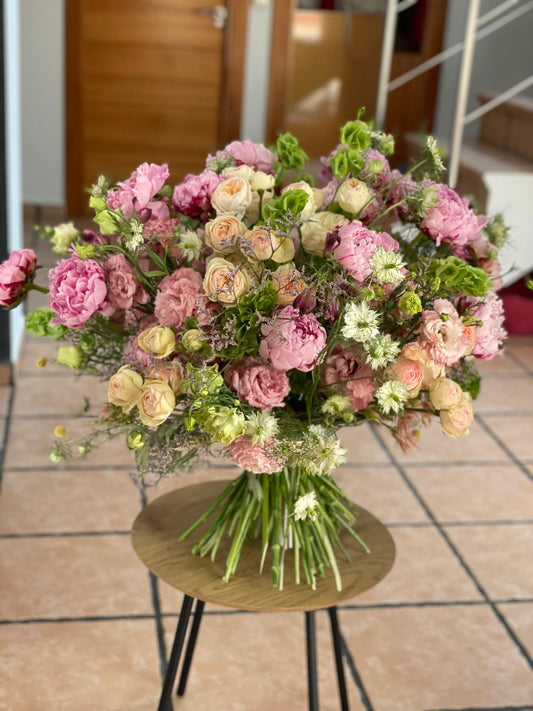Ramo grande de peonías rosas, rosas de jardín crema, lisianthus y nigella sobre mesa redonda