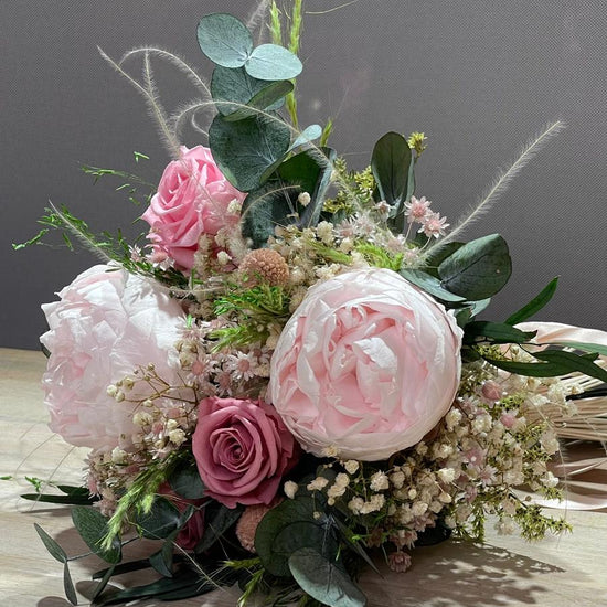Ramo de peonías y rosas rosas con eucalipto, paniculata y hierbas secas, apoyado sobre una mesa de madera