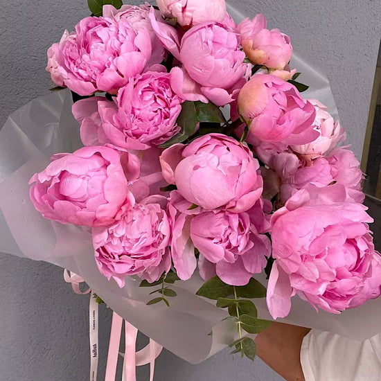 Ramo de peonías rosas con eucalipto, envuelto en papel translúcido con cintas rosas de ANHUÁ Flowers