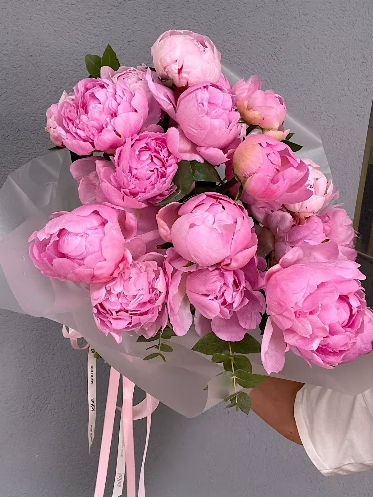 Ramo de peonías rosas con eucalipto, envuelto en papel translúcido con cintas rosas de ANHUÁ Flowers