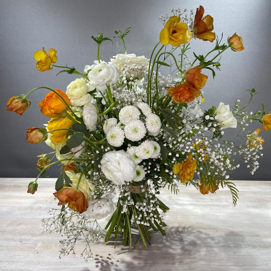 Ramo de ranúnculos naranjas y amarillos con flores blancas sobre mesa de madera