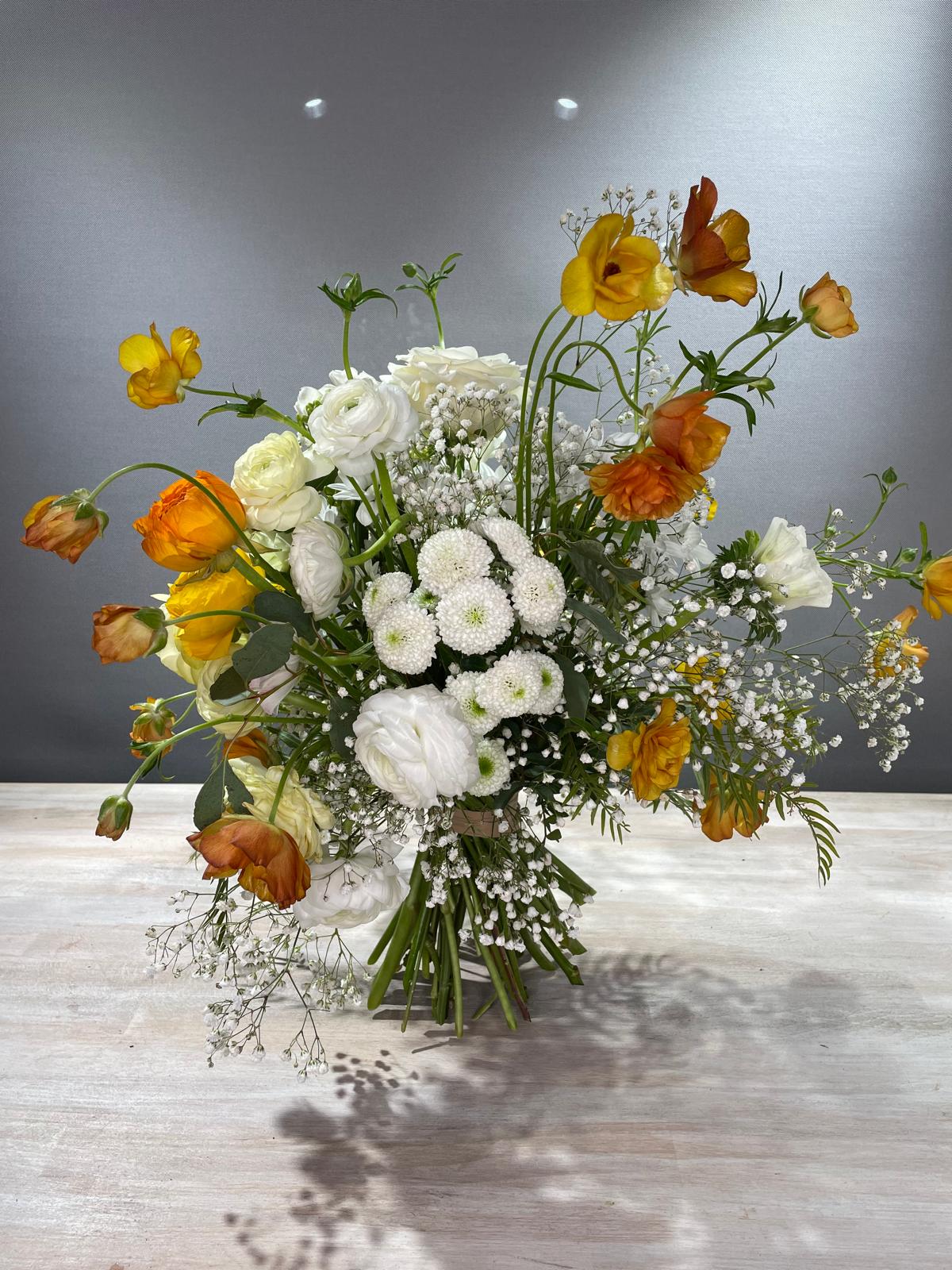 Ramo de ranúnculos naranjas y amarillos con flores blancas sobre mesa de madera