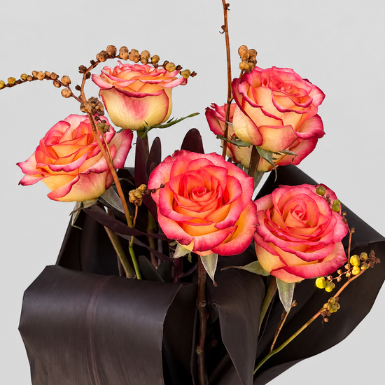 Ramo de rosas bicolor en tonos coral y amarillo con ramas de crocosmia y hojas oscuras en jarrón de cerámica blanca