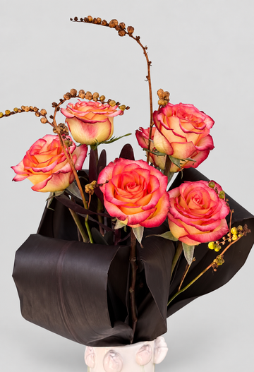 Ramo de rosas bicolor en tonos coral y amarillo con ramas de crocosmia y hojas oscuras en jarrón de cerámica blanca