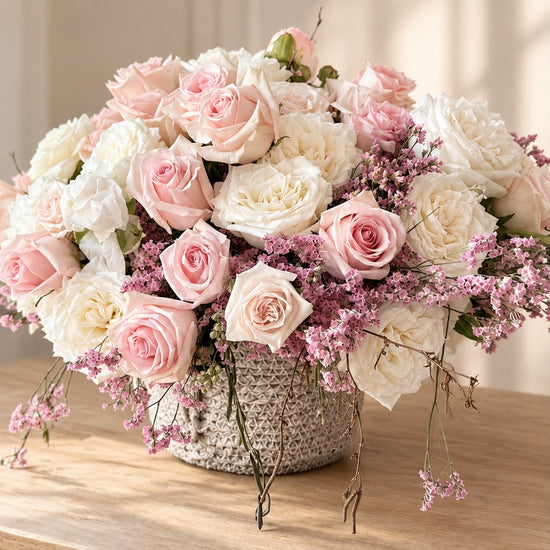 Ramo de rosas blancas y rosas con limonium sobre mesa de madera junto a ventana