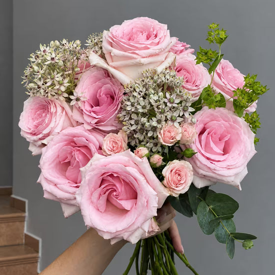 Ramo de rosas rosas y mini rosas con allium blanco, bupleurum y eucalipto, sostenido en la mano