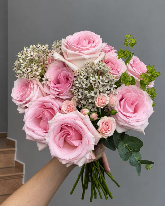 Ramo de rosas rosas y mini rosas con allium blanco, bupleurum y eucalipto, sostenido en la mano