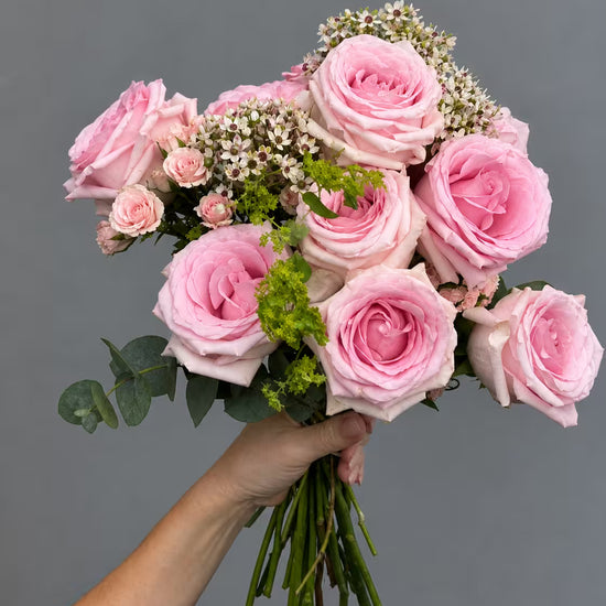 Ramo de rosas rosas con rosas ramificadas, flor de cera, alchemilla y eucalipto, sostenido en la mano