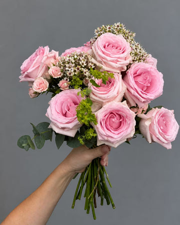 Ramo de rosas rosas con rosas ramificadas, flor de cera, alchemilla y eucalipto, sostenido en la mano