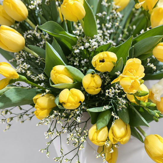 Detalle de ramo de tulipanes y fresias amarillas con limonium blanco y papel de seda blanco