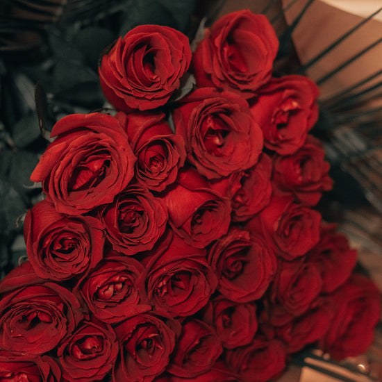 Ramo de rosas rojas con hojas de palma, envuelto en papel marrón
