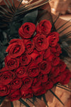 Ramo de rosas rojas con hojas de palma, envuelto en papel marrón