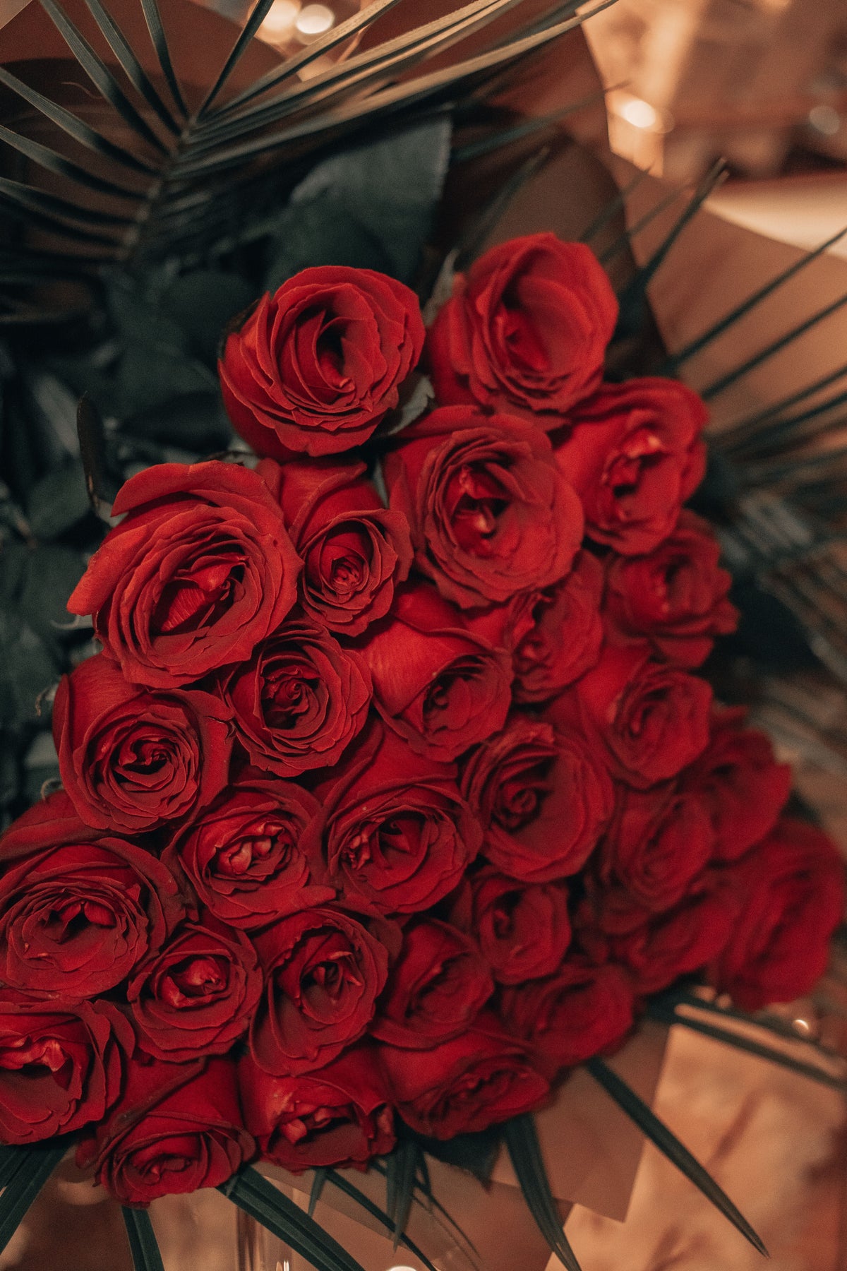 Ramo de rosas rojas con hojas de palma, envuelto en papel marrón