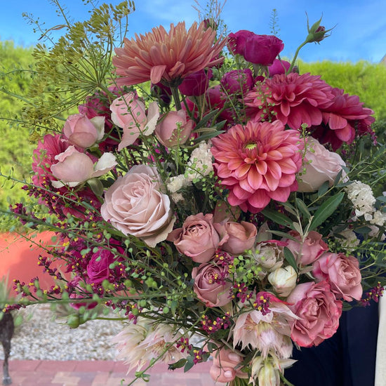 Velours Sauvage — ramo completo con dalias coral, rosas malva y cielo de fondo