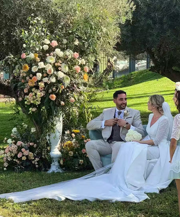 Novios sentados en un sillón al aire libre junto a un arreglo floral grande